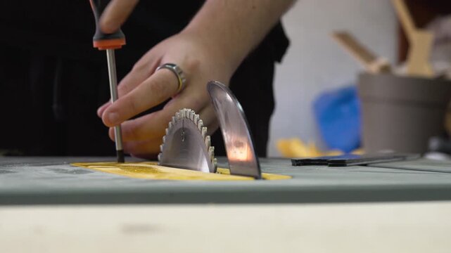 Person removing table saw blade in a workshop setting with focus