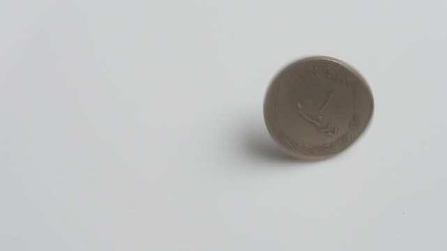 A single silver coin spinning on a white surface before coming to rest. United Arab Emirates one dirham coin AED.