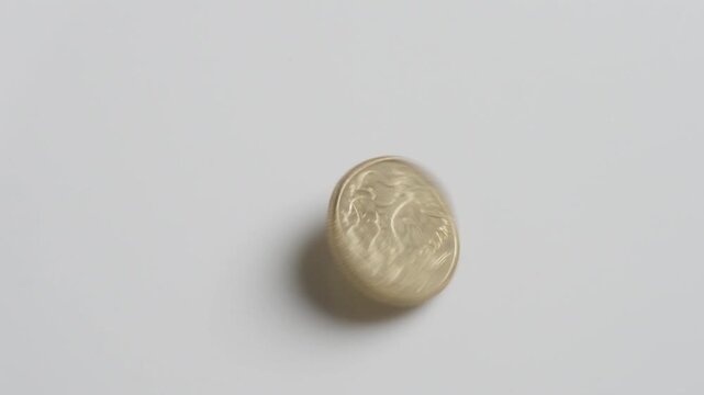 A single gold coin spinning on a white surface before coming to rest. Australian one dollar coin AUD.