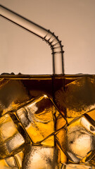 Close-up of a glass with ice cubes and a straw, filled with a dark beverage.