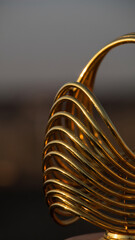 Close-up of a shiny, gold-colored, coiled metal object with a curved handle.