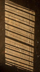Shadow of window bars cast on a dirt ground.