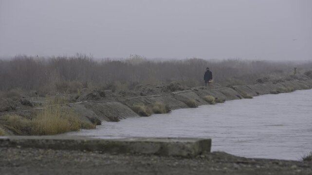 Lone Person Walking on Foggy River Embankment