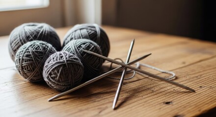 Five yarn balls and crossed needles on a wooden table, near a window. Sunlight