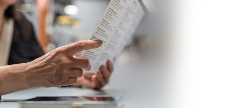 woman hands holding and reading brochure or menu in cafe. Customer reviewing information, choosing product or service with copy space on right side for marketing content.