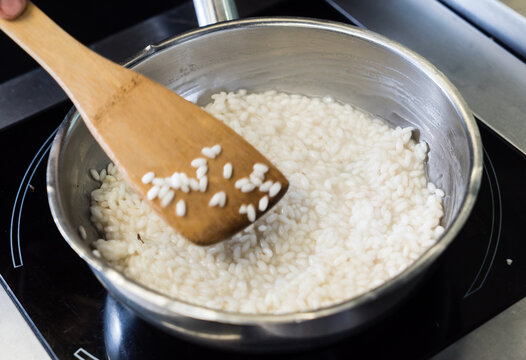 A hand stirs creamy rice gently in a pot, showcasing the art of cooking during a lunch preparations