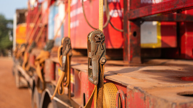 Latching belt strap with metal buckle that securing heavy load on trailer truck to prevent object falling during transportation. Close-up and selective focus.