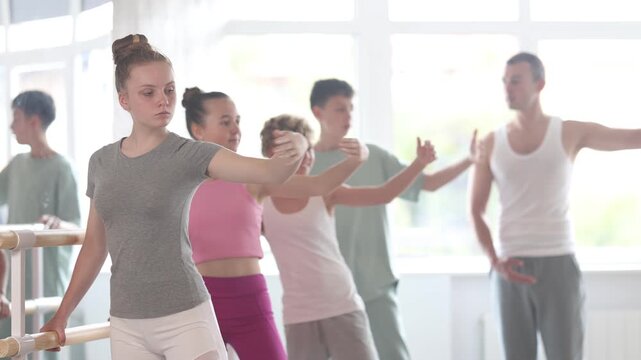 Slim adolescent attendees of ballet courses training battement tendu position under control of ballet-master in dancehall