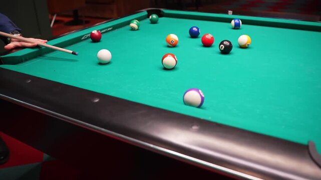 Player aims cue stick at cue ball on green pool table with scattered numbered balls, cinematic bar lighting and shallow depth of field.