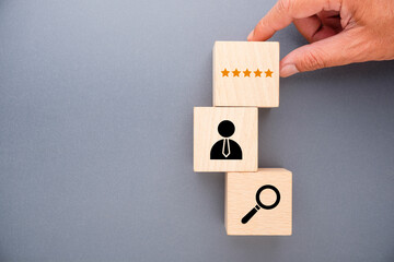Hand stacking wooden blocks with five star rating, employee icon and magnifying glass, representing...