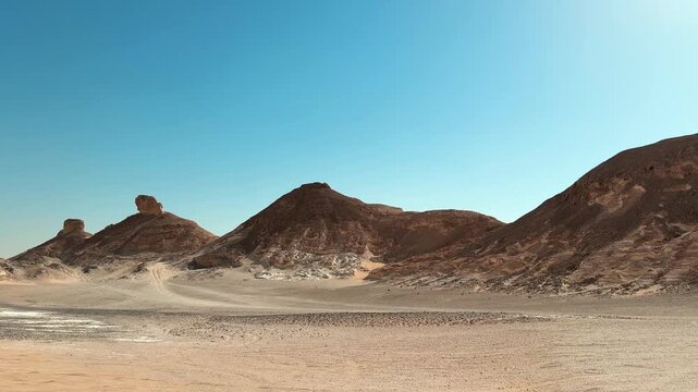 Motion along rocky desert hills rising above flat sandy plain under clear blue sky