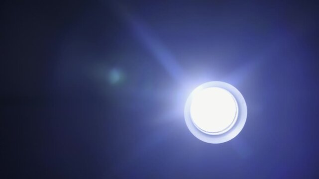Bright circular led light shines on a dark background, creating blue lens flares and a glowing halo. Concept of innovation, electric power, and spiritual illumination.