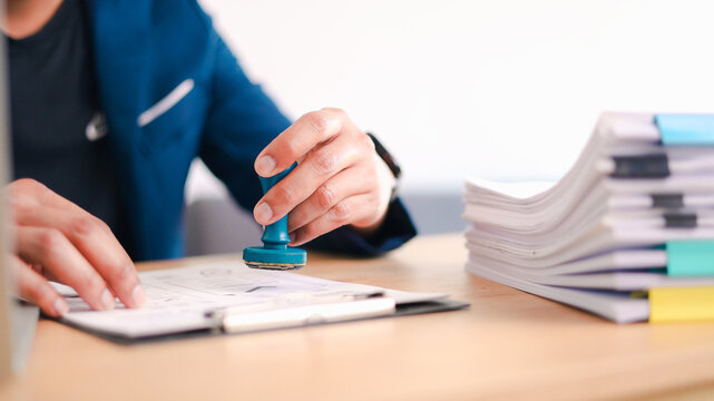 Business professional stamping approved document with official seal at office desk. Concept of contract approval, legal authorization, compliance verification.