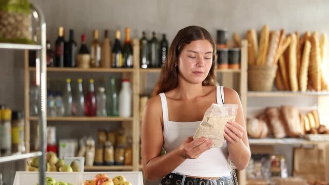 Young female shopper chooses oat flakes in package in grocery store