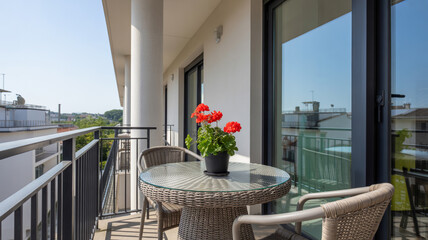 Fototapeta premium A bright balcony features a small table chairs and vibrant red geraniums