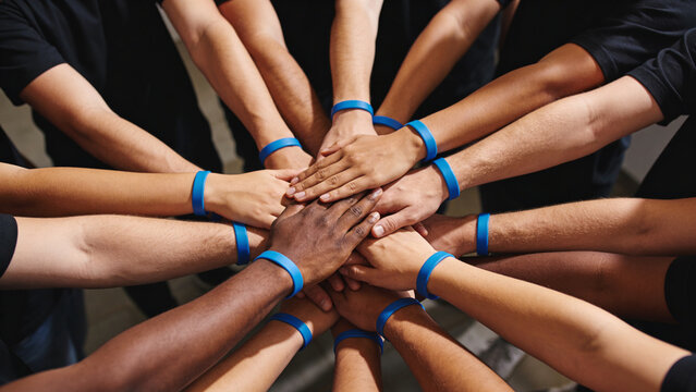 Diverse group of people hands stacked together wearing blue wristbands symbolizing unity and teamwork