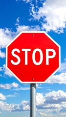 Obraz premium Red stop sign against a blue sky with white clouds. Vertical, centered composition