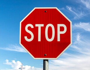 Obraz premium Red stop sign with white letters against a blue, partly cloudy sky, mounted on a metal pole