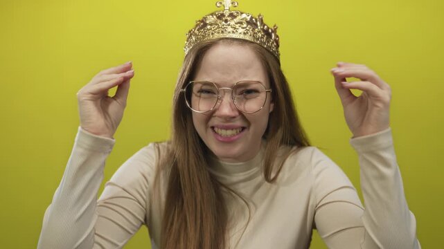 Woman wearing crown and glasses raises hands with open mouth in studio against chartreuse wall; frustration.