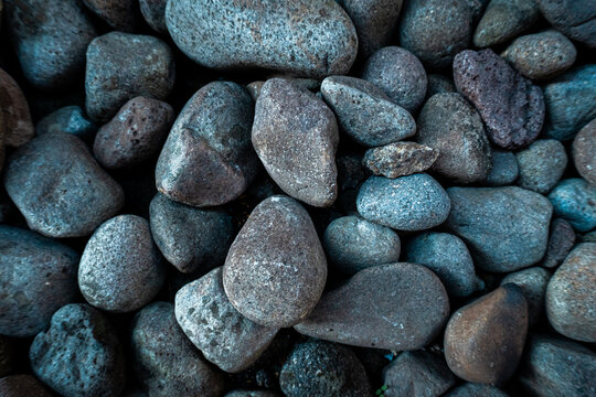 Collection of smooth, water worn river rocks and pebbles arranged closely, creating a natural and rough surface texture in varying shades of grey and earthy tones