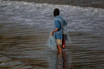 A Thai fisherman with a net catches fish in the coastal area on a sunny morning