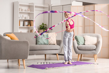Cute girl with ribbon doing gymnastics at home