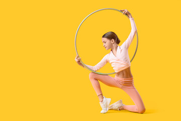 Cute girl with hula hoop doing gymnastics on yellow background