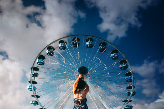 Girl Standing in front of Ferris Wheel with Cloudy Sky in Background