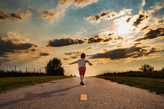 Boy Running Down Walking Path with Cloudy Sky