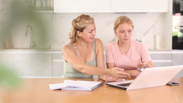  Mom helps her teenage daughter to do her homework and looks carefully at childs notebook. Female tutor performs difficult educational task with child.
