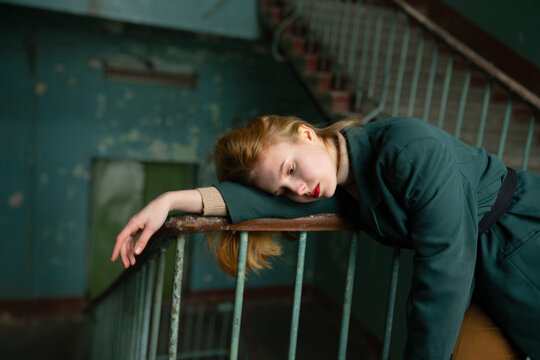 Teenage girl with red hair in green jacket leaning on handrail in old entrance