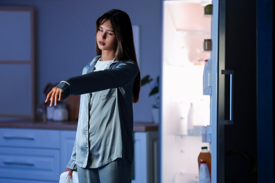Female sleepwalker near fridge in kitchen at night