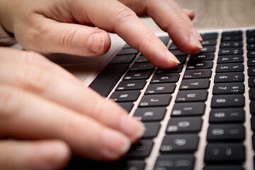 Close-up of female hands typing on a modern laptop keyboard in a home office.