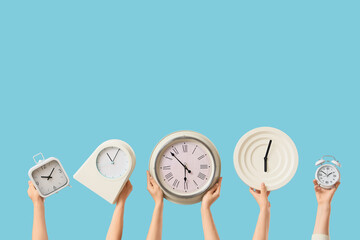 Female hands holding different wall and alarm clocks on blue background