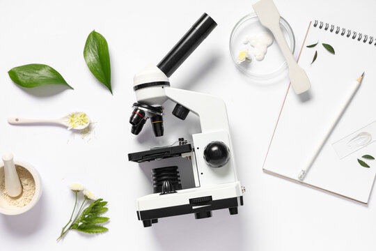Botanical laboratory research flat lay with microscope medicinal plant leaves flowers cream petri dish mortar and pestle on white background