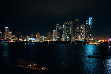 Obraz premium Illuminated Miami Skyline at Night, Iconic Skyscrapers Reflecting in Biscayne Bay with Vibrant Neon Lights