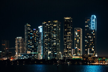 Obraz premium Illuminated Miami Skyline at Night, Iconic Skyscrapers Reflecting in Biscayne Bay with Vibrant Neon Lights