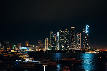 Obraz premium Illuminated Miami Skyline at Night, Iconic Skyscrapers Reflecting in Biscayne Bay with Vibrant Neon Lights