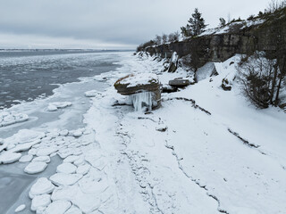 High angle drone view of Vaike-Pakri island rocky coast with limestone cliffs and frozen sea during winter in Estonia.
