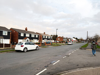 Fototapeta premium Residential street in Manchester UK with a white car parked along the curb and a pedestrian