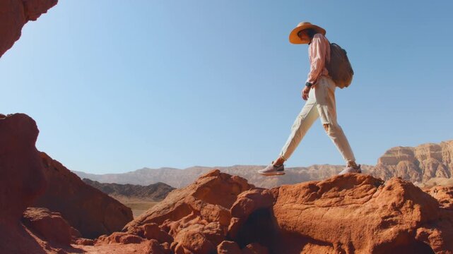 A woman with a backpack walks through dry sandy terrain, exploring the surroundings of the desert. Trekking and hiking in the desert. Adventure and travel.