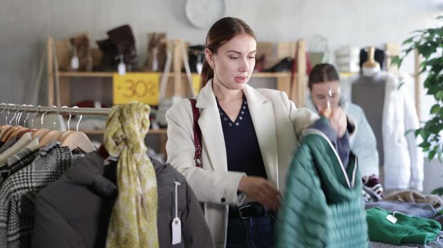 Pleased young female customer holding a hanger with puffer jacket in clothing-store on Black Friday