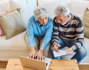 Senior couple checking bills and calculating expenses using a laptop at home, debt taxes concept,...