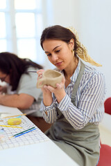 Focused Woman Crafting Clay Vessel in Bright Studio During Pottery Workshop