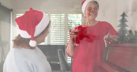 Chatting senior woman in red-top Santa-hat holding wine glass in living-room by piano, shutters © vectorfusionart