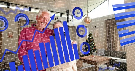 Smiling senior couple wearing red shirt standing at home with blue data overlay, Christmas tree