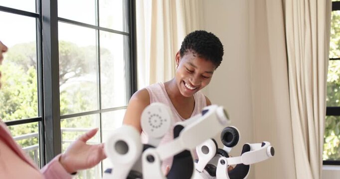 Two adult women at home, left presenting parts African-American pale-pink top testing multiarm unit