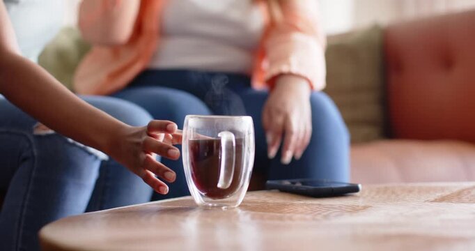 Left hand is reaching as two women are lifting and testing mugs for temperature on couch