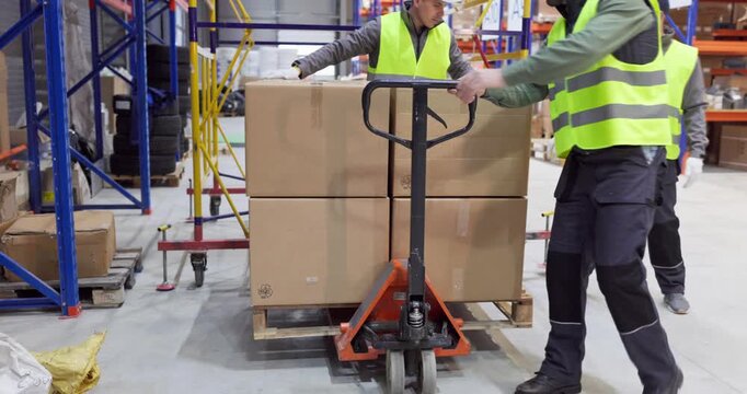 Warehouse workers moving boxes with pallet truck. Warehouse team moves a pallet through aisles for delivery, shipping, and order fulfillment. Strong concept of efficient teamwork logistics.