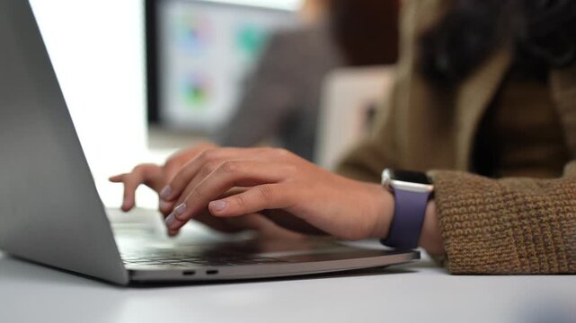 Young woman&rsquo;s hands typing on a laptop keyboard, composing emails and messages while working on a project in a bright modern office with screen blurred in the background